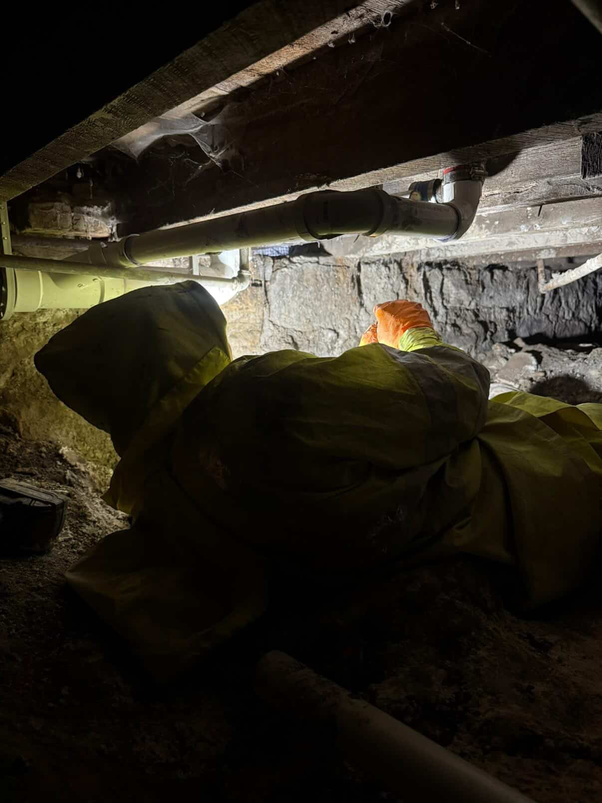 Plumber working in tight crawlspace on overhead drain line